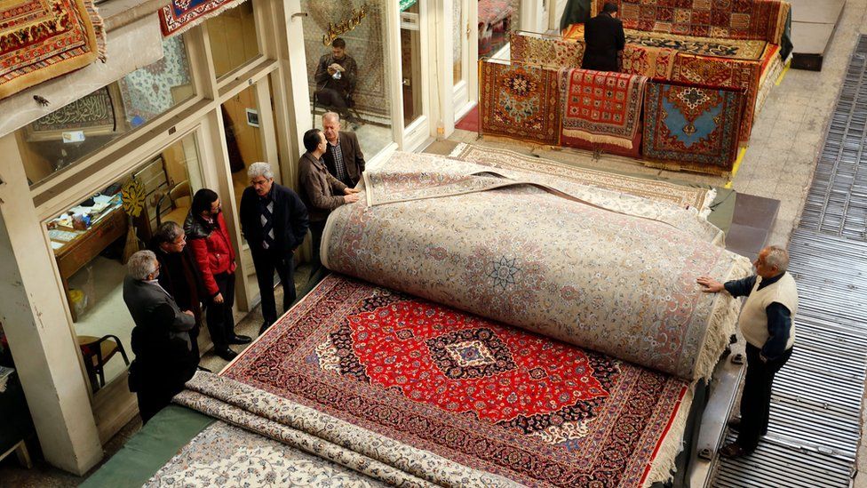 Shoppers and carpet sellers stand next to carpets in Tehran's Grand Bazaar in Iran.