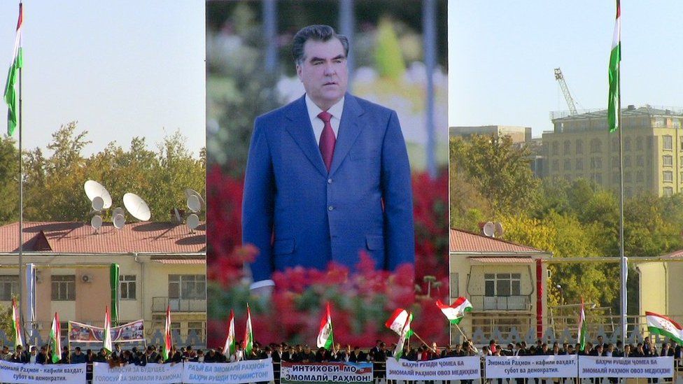 People wave flags in front of an image of President Emomali Rakhmon