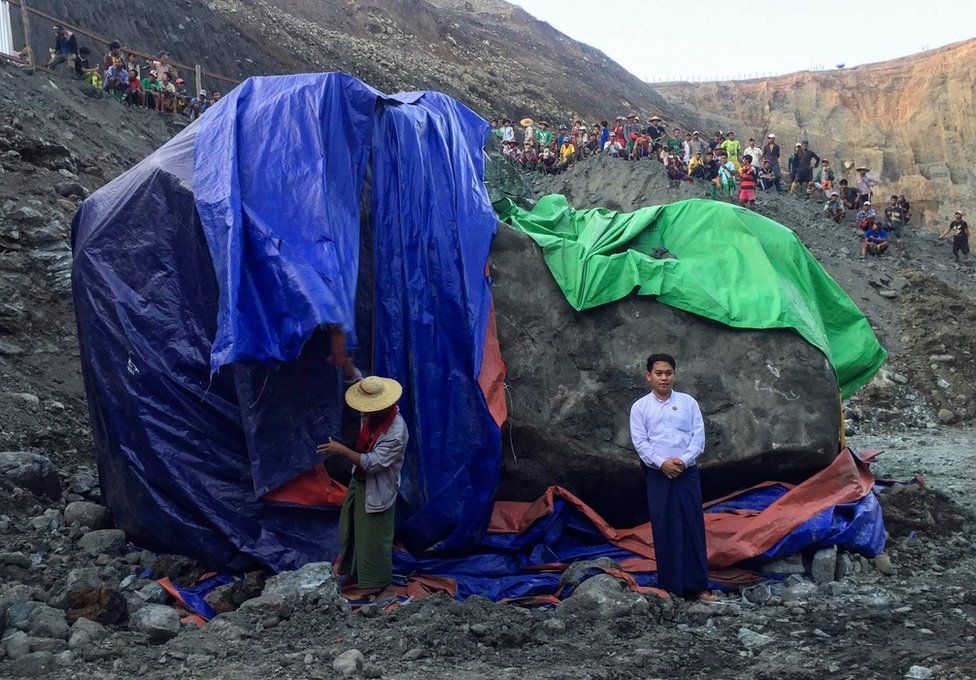 A man poses for photographs next to a worker preparing to cover the giant jade stone as miners gather and watch at a mine in Phakant, Kachin State, northern Myanmar