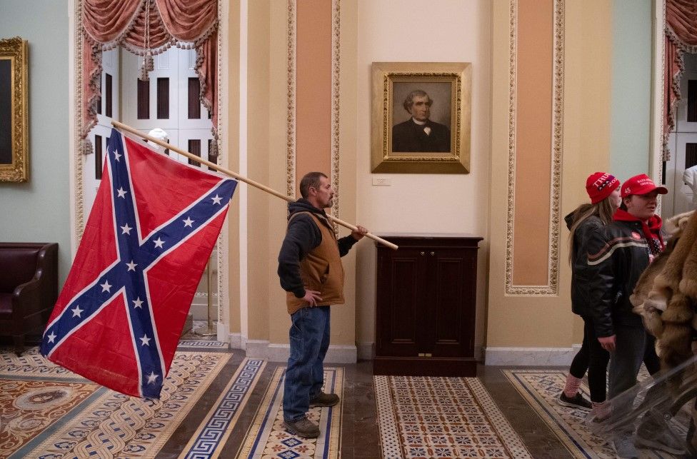 Un partidario de Trump sostiene una bandera confederada afuera de la Cámara del Senado