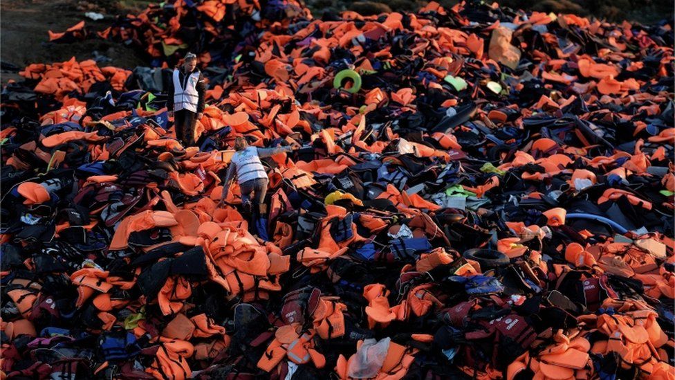 Volunteers stand on a pile of lifejackets left behind by refugees and migrants who arrived to the Greek island of Lesbos