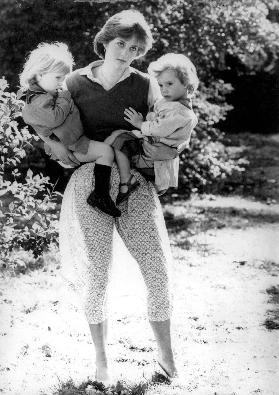 Diana holds two children as the sun shines through her skirt.