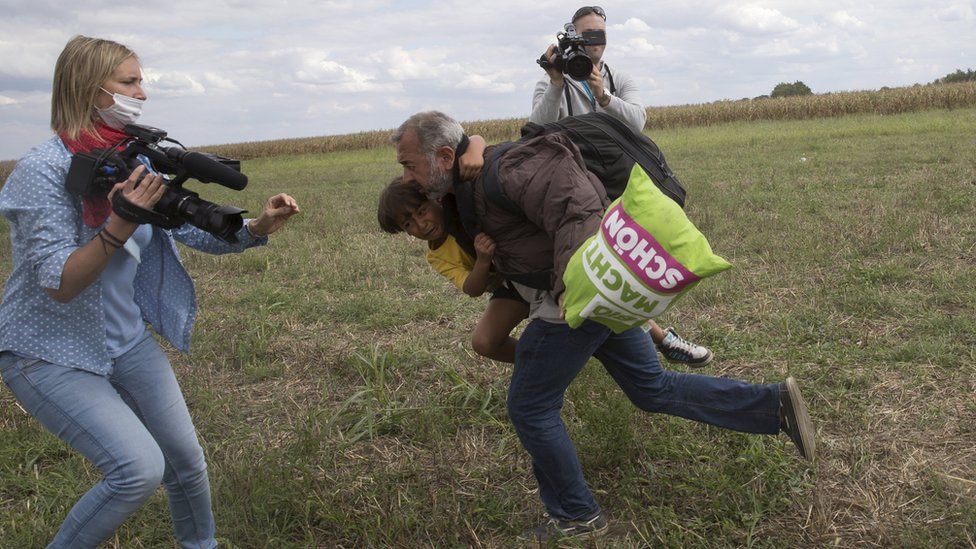 A man runs with a child before tripping on TV camerawoman Petra Laszlo (L) and falling