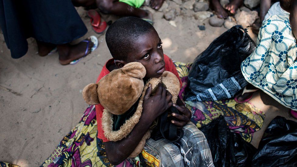 A boy holds his teddy bear as he waits with other Internally Displaced Persons (IDP) for a daily food ration at a camp for people fleeing the conflict in the Kasai province on 7 June 2017 in Kikwit.