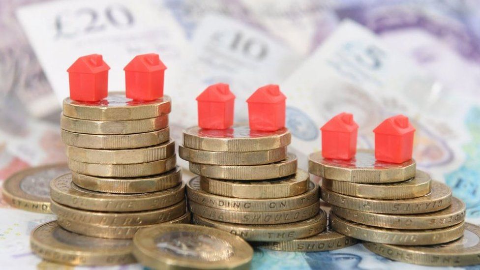 An image showing plastic monopoly houses sitting on pound coins and banknotes