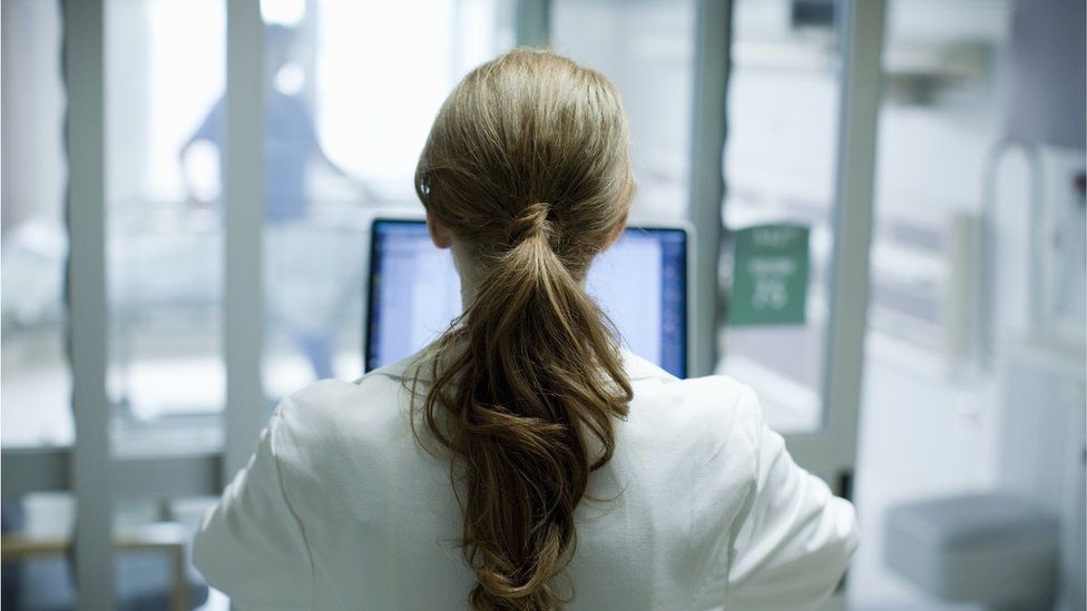 Woman in a medical lab coat facing a laptop