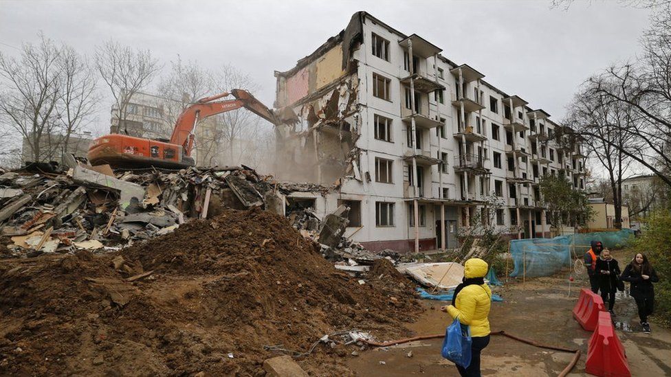 A women watches as excavator and workers demolish a five storey khrushchyovka building in Moscow