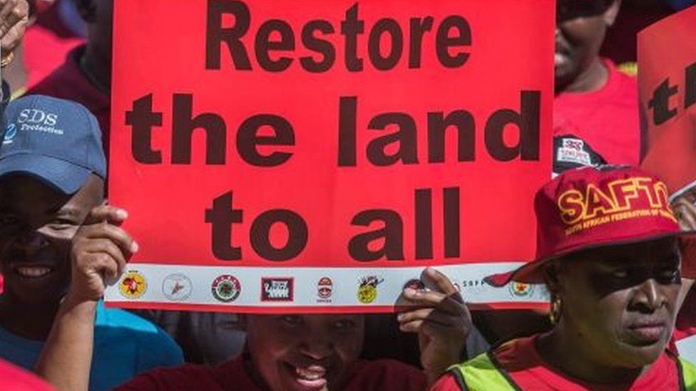 A demonstrator in South Africa holds a placard reading "Restore the land to all" as thousands of workers take part in a national strike called by the country's second largest labour union - April 2018