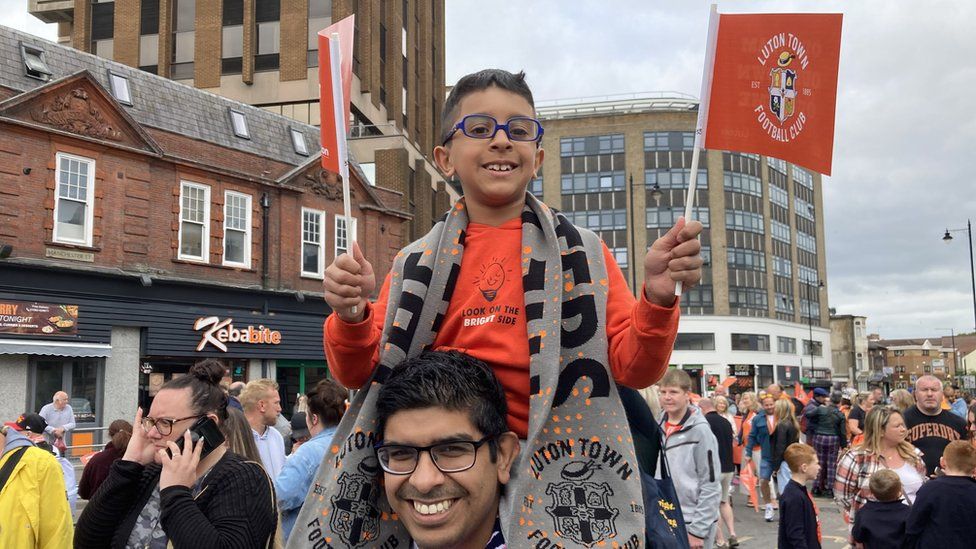 A young boy on the shoulders of a man celebrating in Luton town centre