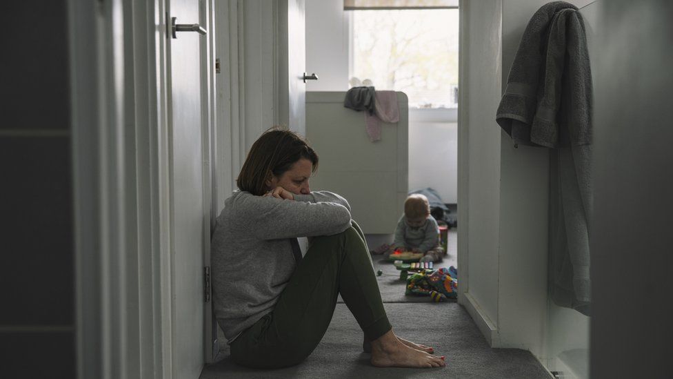 Woman looking distressed sits on carpeted floor of home as child plays in background (file image)