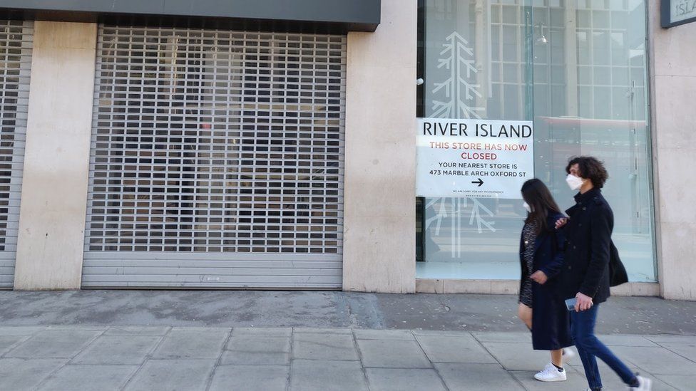 Two people walk past a boarded up River Island store on Oxford Street