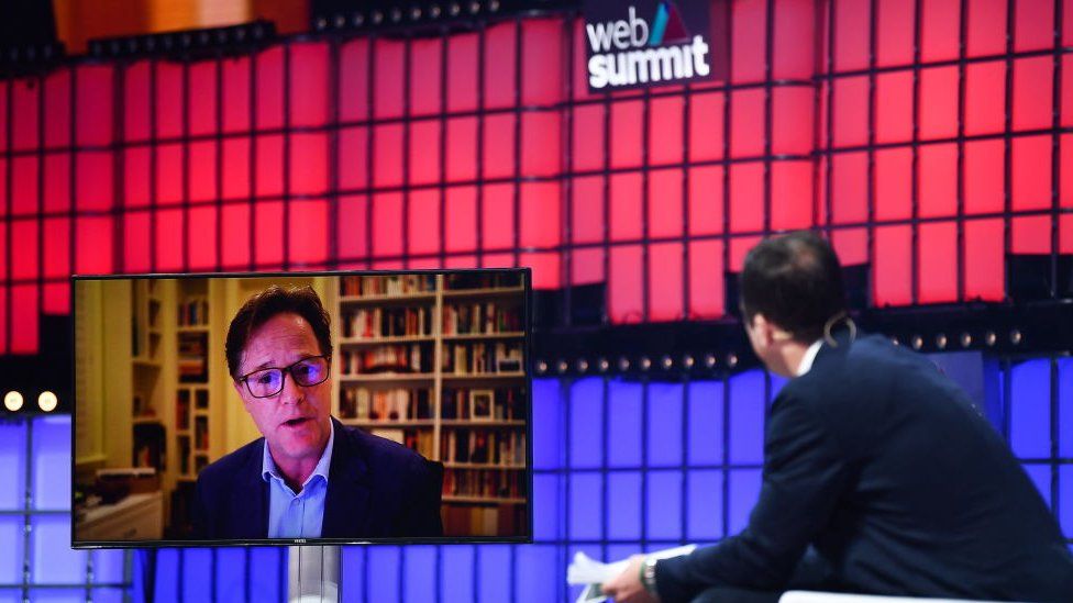Sir Nick Clegg appears on a video screen on a stage in conversation with a host