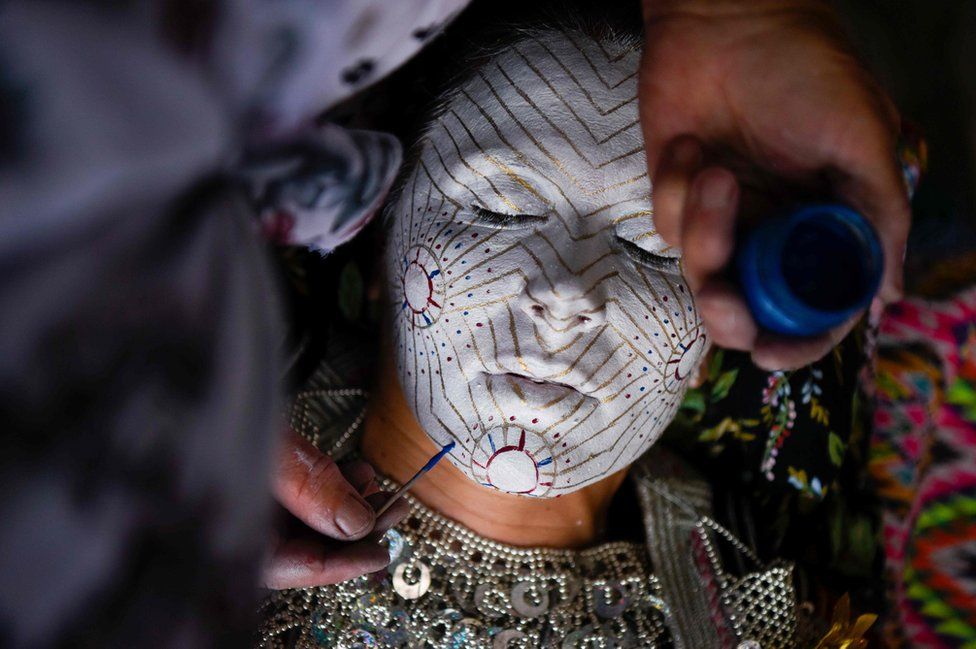 Kosovar woman Sheqerie Buqaj lays on her back as she receives a traditional face painting