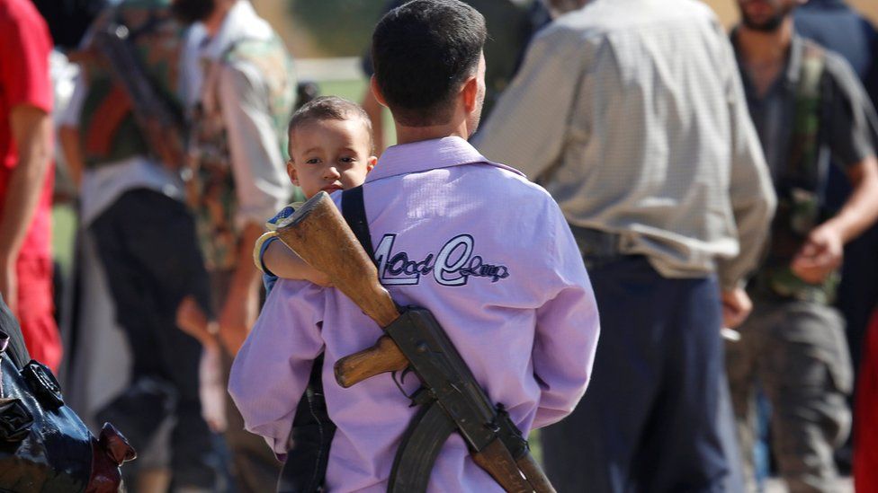 A Syrian rebel armed with a gun holds a child