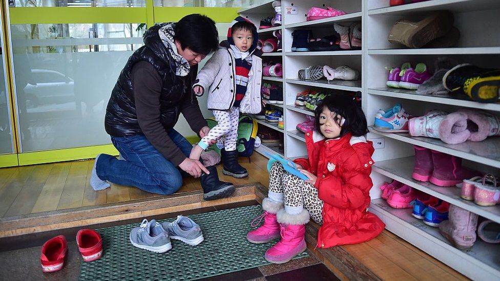 Южнокорейский отец надевает обувь на сына, а его дочь смотрит на детский сад в Сеуле 22 декабря 2015 года