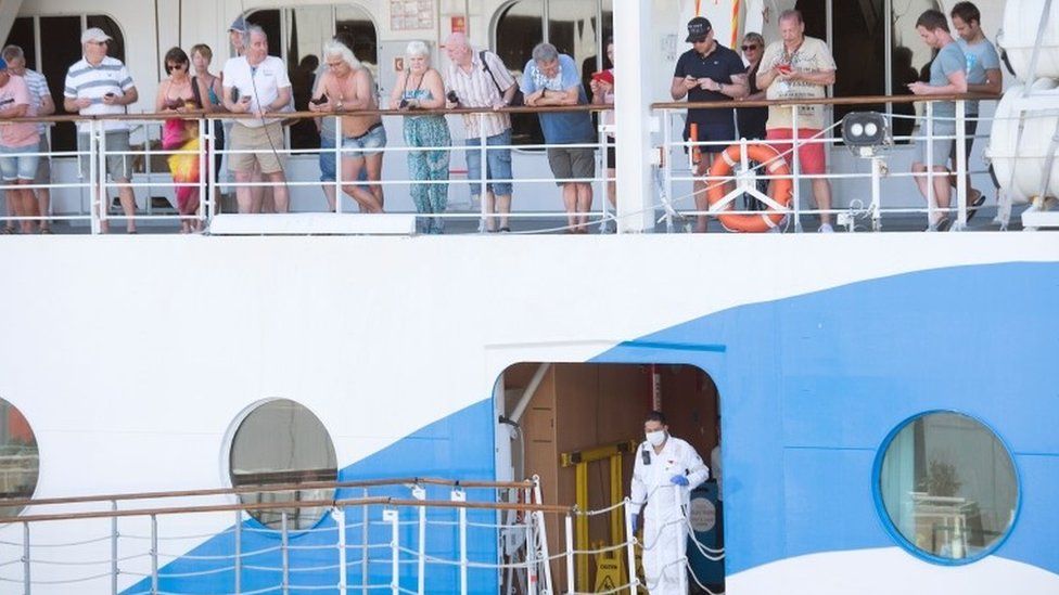 People wait around on the AIDAmira, an Italian registered cruise ship carrying mostly German passengers, as the ship is docked in Cape Town harbour, and is being quarantined due to several suspected COVID-19 cases on board, on March 18, 2020, in Cape Town.