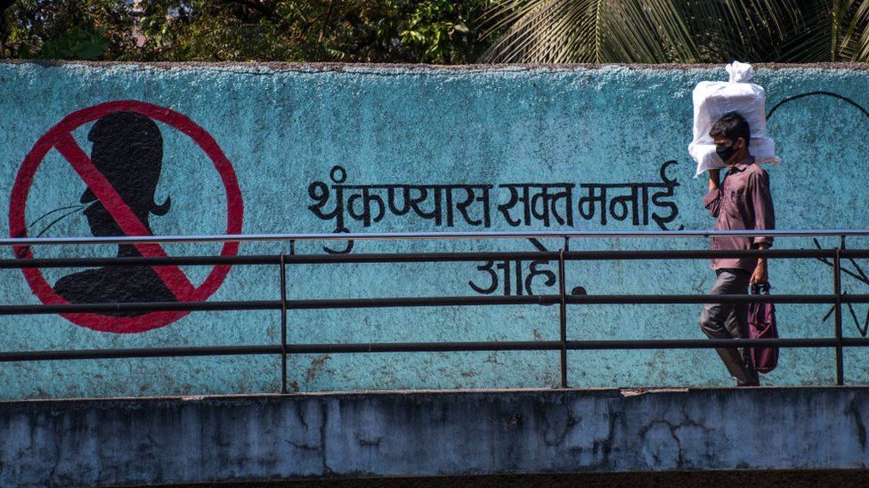 Мужчина в маске в качестве защиты от вируса короны проходит рядом с надписью «Не плевать» на стене в Marinelines 18 марта 2020 года в Мумбаи, Индия.