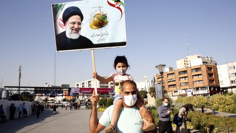 Girl on a man's shoulders holds up a poster of election candidate Ebrahim Raisi