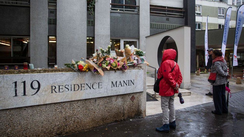 Members of the public stand in front of bunches of flowers displayed outside the building in Paris on October 17, 2022