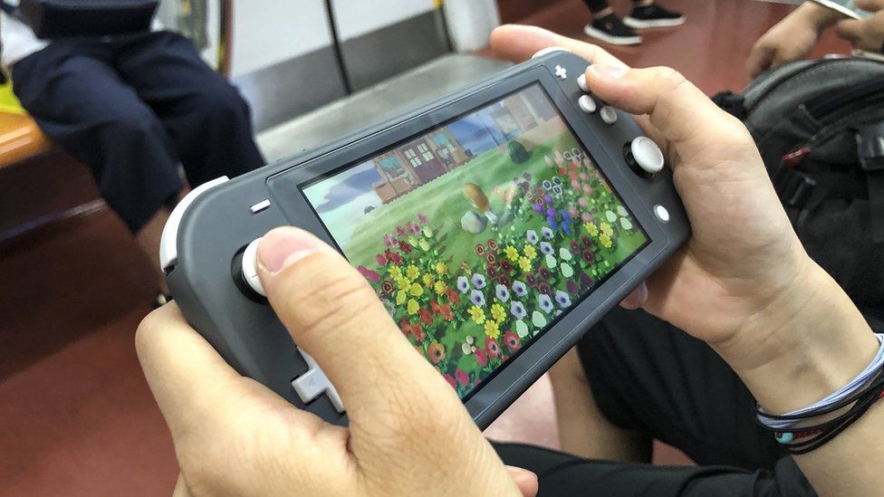 The hands of a person are seen playing Animal Crossing on the Nintendo Switch while on some form of train or underground transport