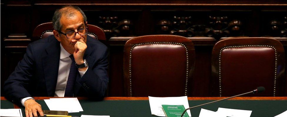 Italian Economy Minister Giovanni Tria, pictured alone, muses in Italy's dark oak and red leather parliament chamber