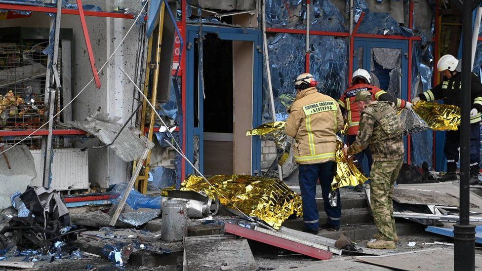 Rescuers holding thermal blankets in front of a building with shattered windows