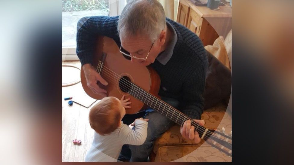 Man playing an acoustic guitar while a baby looks up