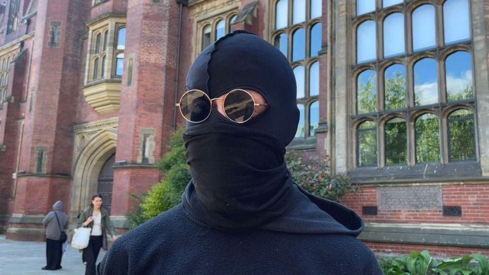 The spokesperson for the protesters wearing a balaclava and sunglasses