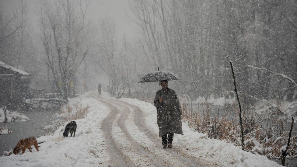 Мужчина с зонтиком идет по заснеженной дороге во время снегопада в Шринагаре. В Кашмирской долине прошел свежий снегопад, нарушивший нормальную жизнь людей. Полеты, наземный транспорт и рутинная повседневная жизнь прекратились. Электричество также пострадало во многих районах Кашмира. Администрация Джамму и Кашмира в понедельник объявила о высоком уровне опасности схода лавин в нескольких регионах в ближайшие 24 часа.