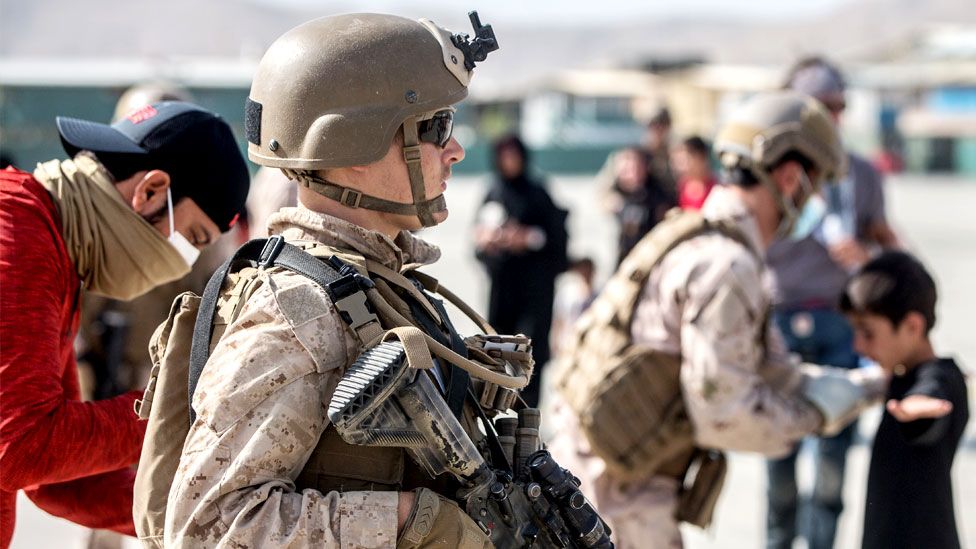 A US Marine provides assistance during an evacuation at Hamid Karzai International Airport, Kabul, Afghanistan, 21 August 2021