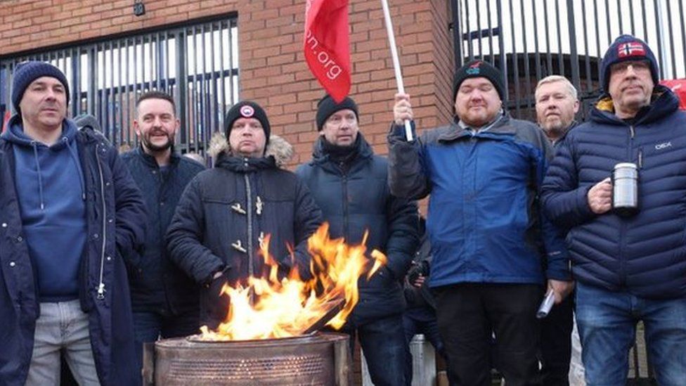 men keeping warm around a fire while flying Unite the Union flags