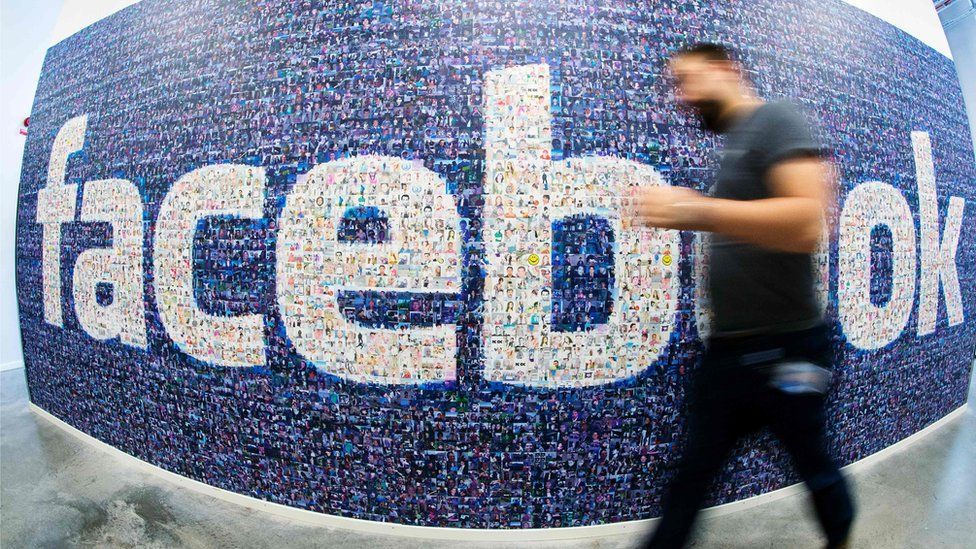 Man walking in front of a mural of Facebook users