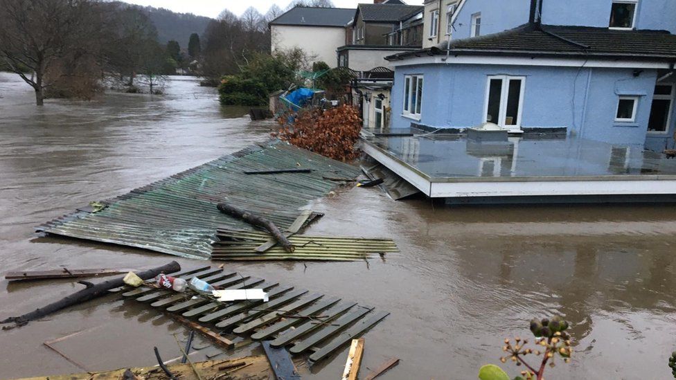 Flood water, carrying debris such as corrugated iron sheets and wooden pallets, up to the second floor of a house