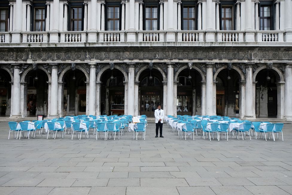 A waiter stands by empty tables outside a restaurant at St Mark's Square after Italy's government adopted a decree with emergency new measures to contain the coronavirus, in Venice. March 5, 2020.