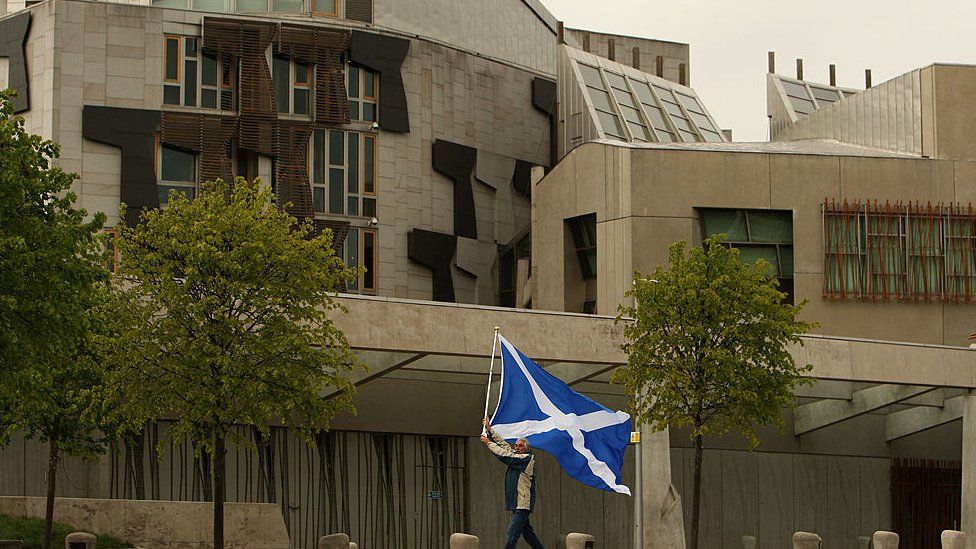 A man holds a Saltire flag outside the Scottish Parliament