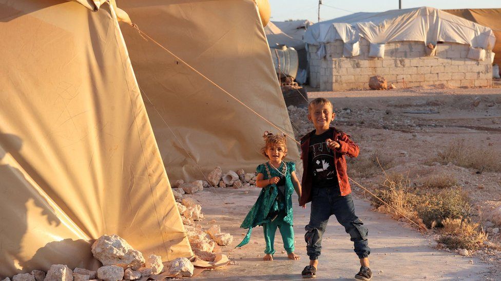 Children walk outside a tent at the "Blue Camp" for Syrians displaced by conflict near the town of Maaret Misrin in rebel-held Idlib province (10 July 2022) during the Muslim holiday of Eid al-Adha on July 10, 2022