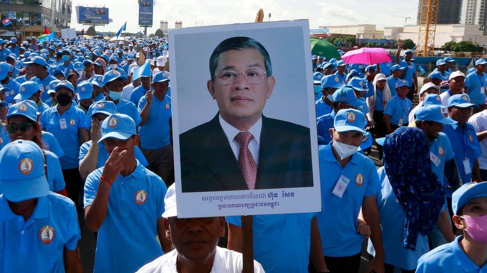 A crowd of ruling party supporters wearing blue uniforms and hats march in Phnom Penh on 1/7 in support of Hun Sen, with one carrying a large placard bearing the PM's picture