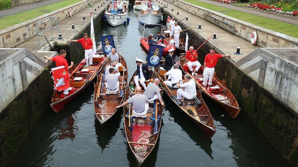 Six rowing boats with swan uppers onboard wait in a river lock