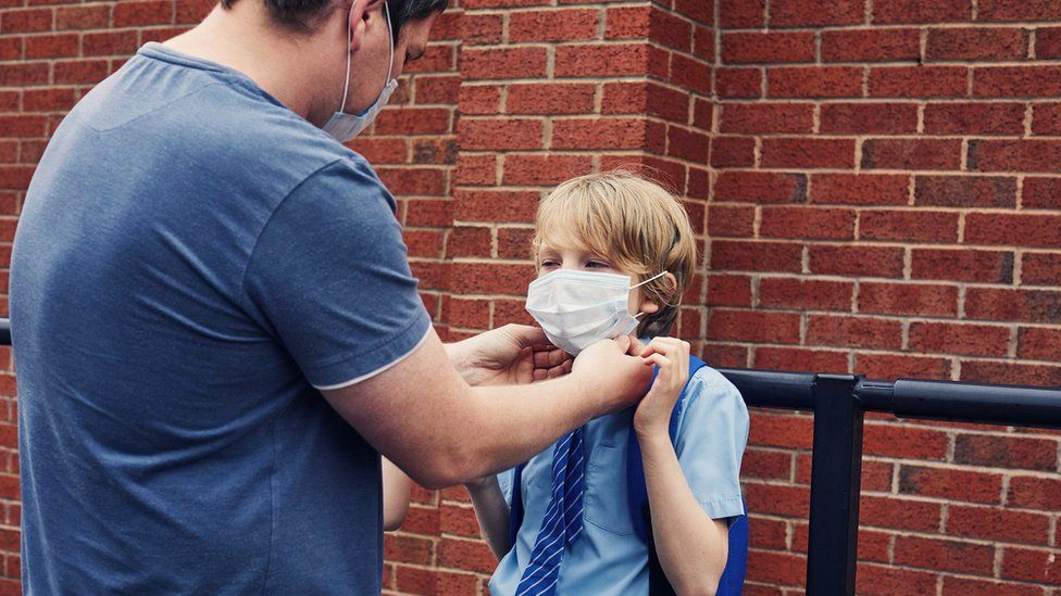 father putting mask on son in school uniform