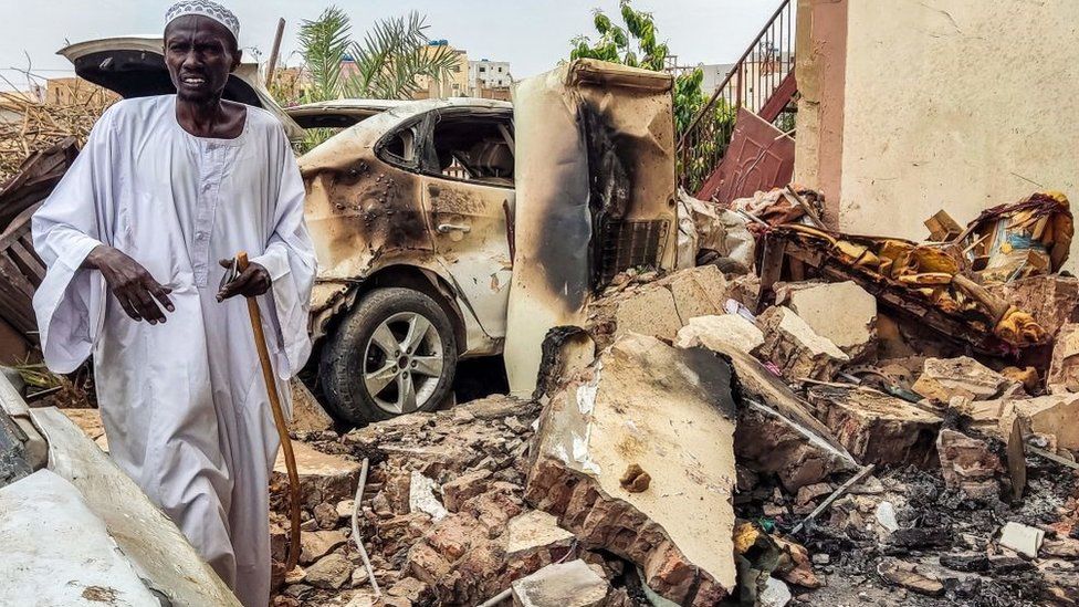 A man inspects damage as he walks through the rubble by a destroyed car outside a house that was hit by an artillery shell in the Azhari district in the south of Khartoum on June 6, 2023