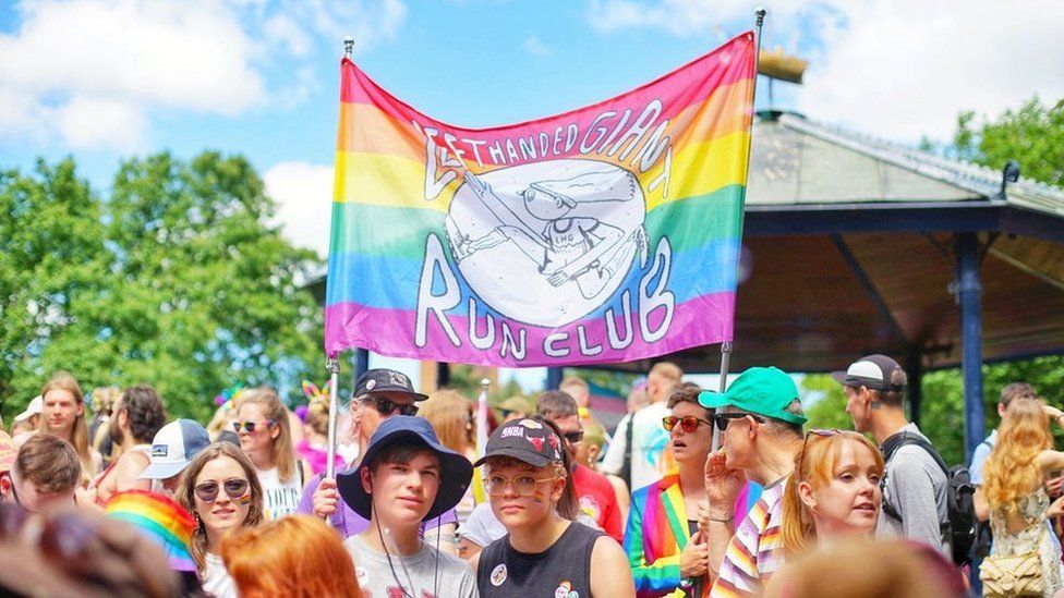 People standing underneath a Left Handed Giant Run Club flag at Bristol Pride