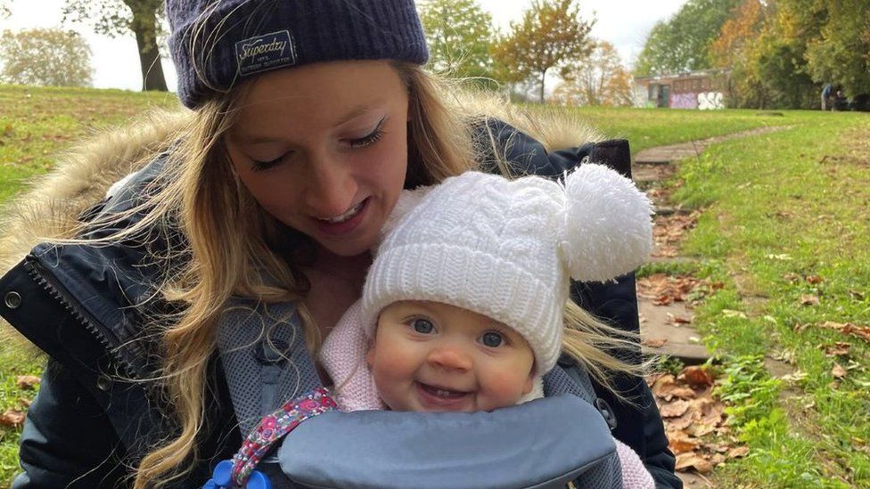 Charlotte and Maya in a pappouse both wearing woolly hats and smiling on a walk