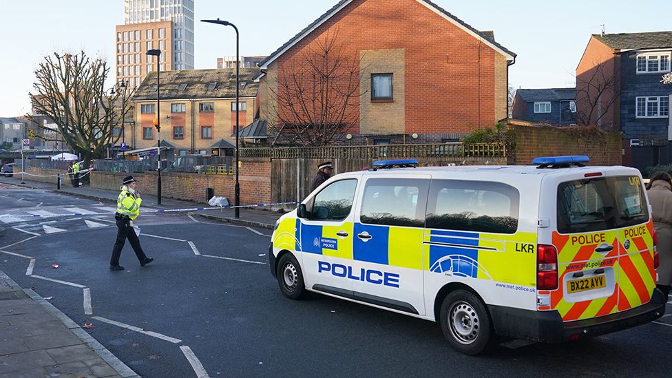Police van and police officer are seen on the road with residential buildings in the background, in Hackney on 6 December