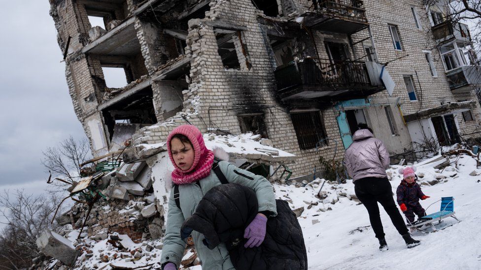 Familie vor zerstörtem Gebäude in Izyum