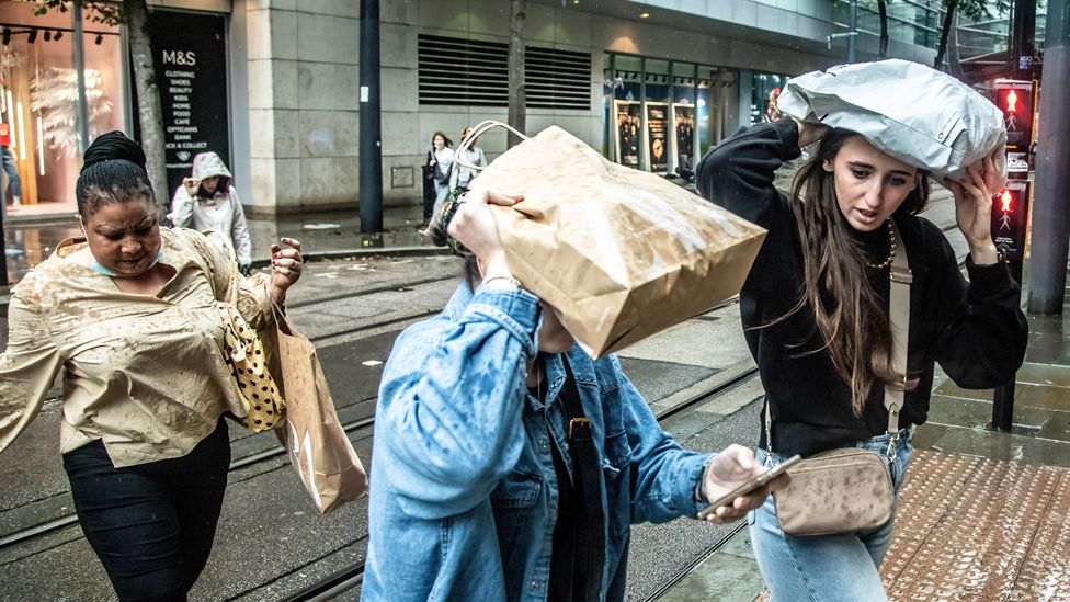 Women walk along while covering themselves with shopping bags during a rainy day in Manchester