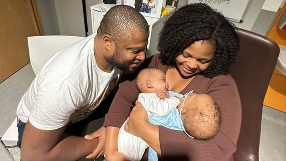 Dad Christian looks at twins being held by Mum Primrose