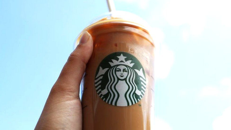 A person holds a Starbucks drink in the air.
