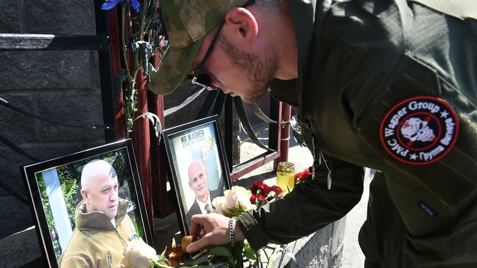 A Wagner fighter leaves a tribute in front of portraits of Wagner leaders Yevgeny Prigozhin and Dmitry Utkin at the group's offices in Novosibirsk