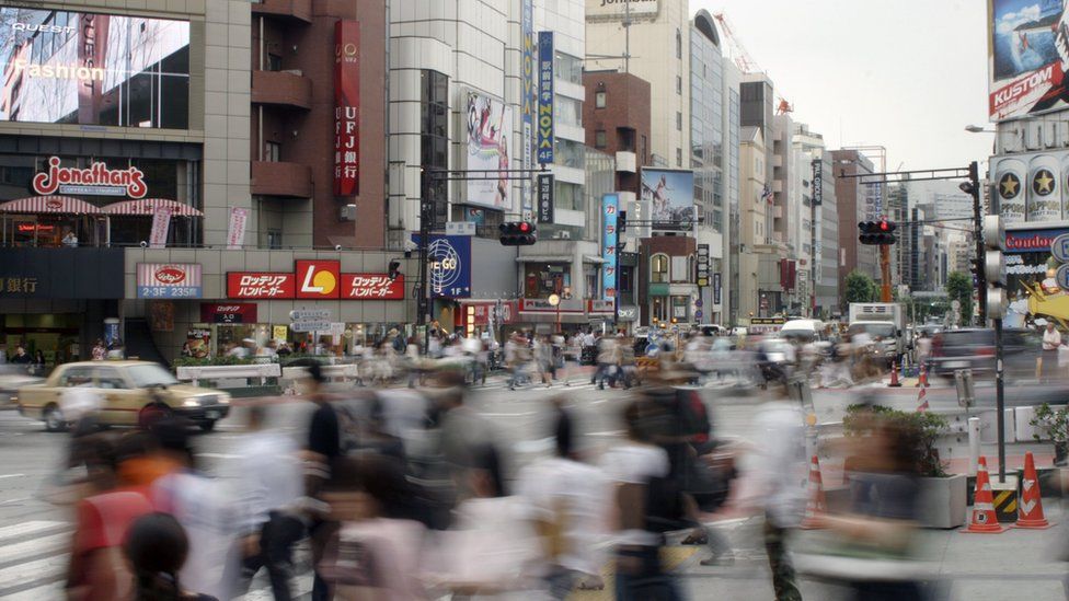 A blurred image shows the motion of busy commuters in downtown Tokyo, Japan