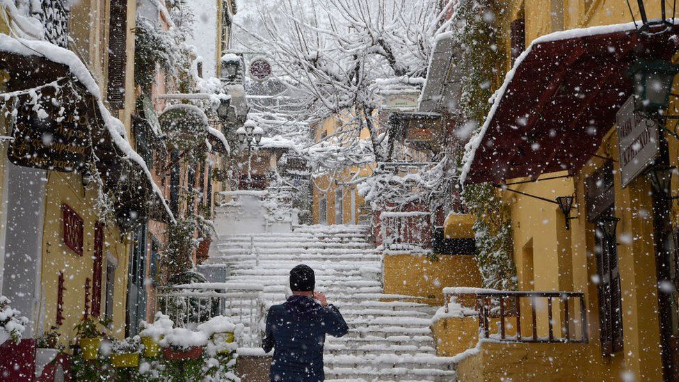 Мужчина фотографирует в популярном туристическом районе Плака во время сильного снегопада в Афинах